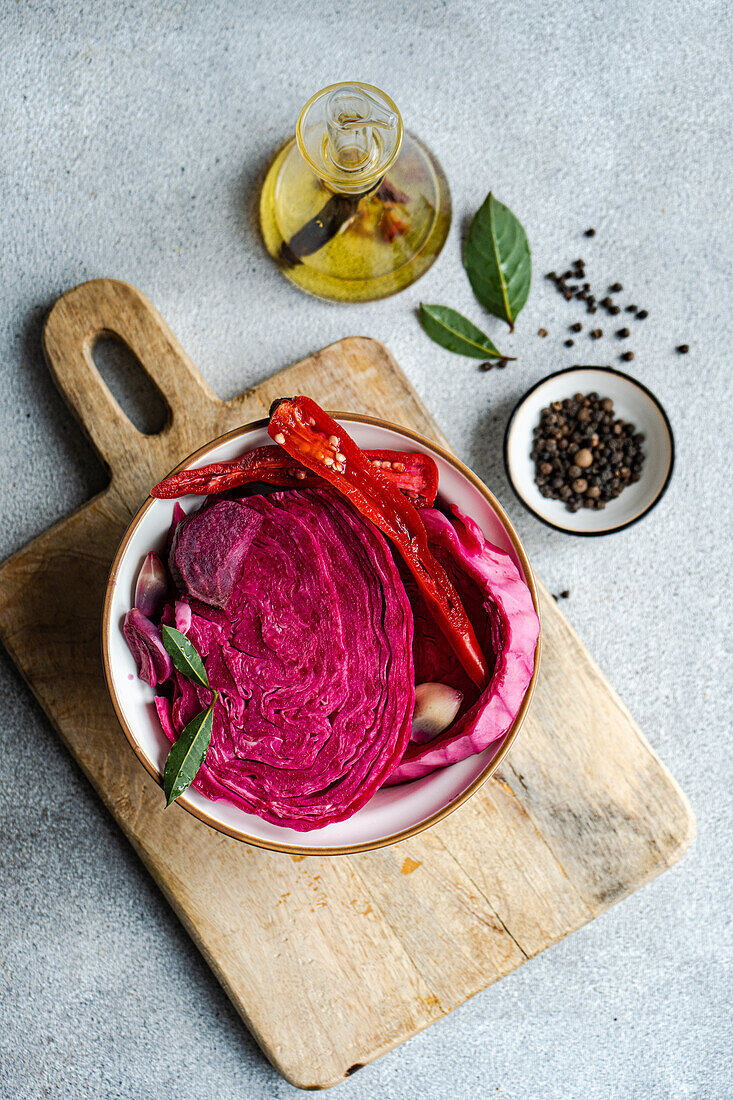 A top-down view of fermented cabbage with beetroot, garnished with spicy red pepper, garlic, and bay leaves, served in a bowl on a wooden board.