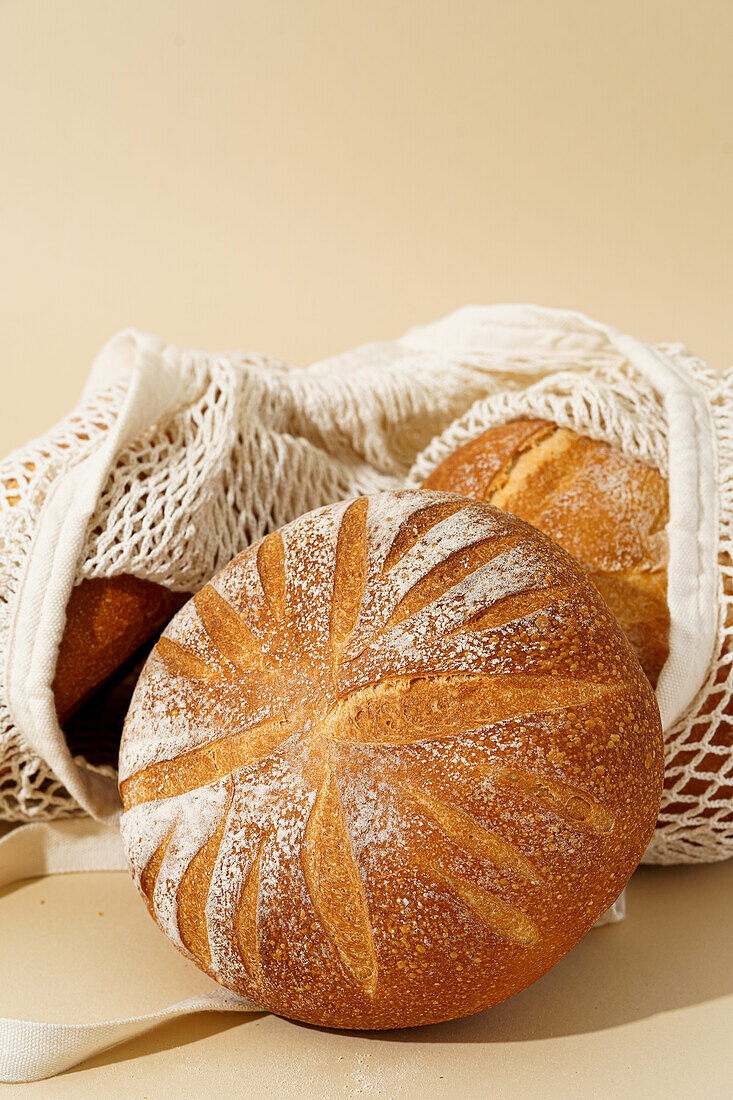 Artisanal sourdough breads with a golden crust, displayed in an eco-friendly cloth bag against a beige background.