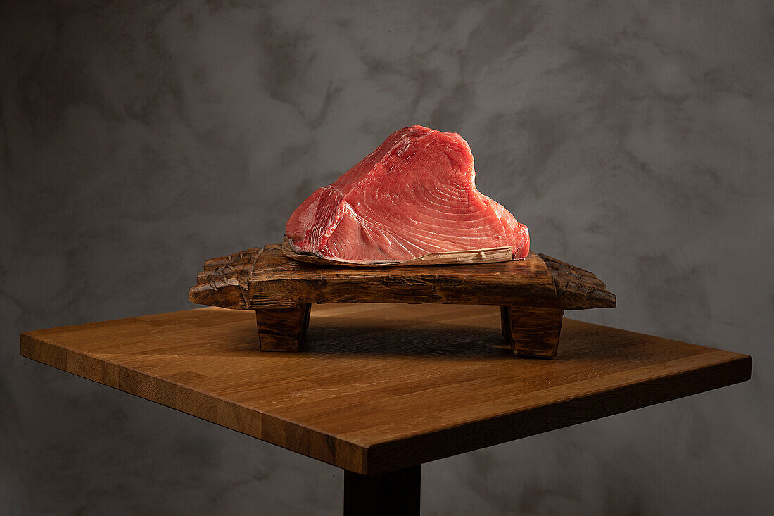 A high-quality raw tuna steak displayed on a rustic wooden cutting board, set against a dark, textured backdrop, ideal for sushi preparation themes