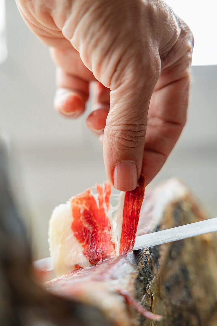 A close-up image of a hand skillfully slicing a thin piece of Iberian ham The marbling and texture of the meat are showcased, capturing the craftsmanship and tradition of this gourmet delicacy