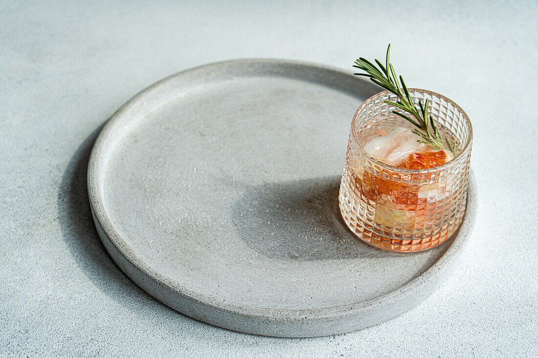 A modern take on the classic vodka tonic, featuring a grapefruit slice and rosemary garnish, displayed on a smooth concrete tray