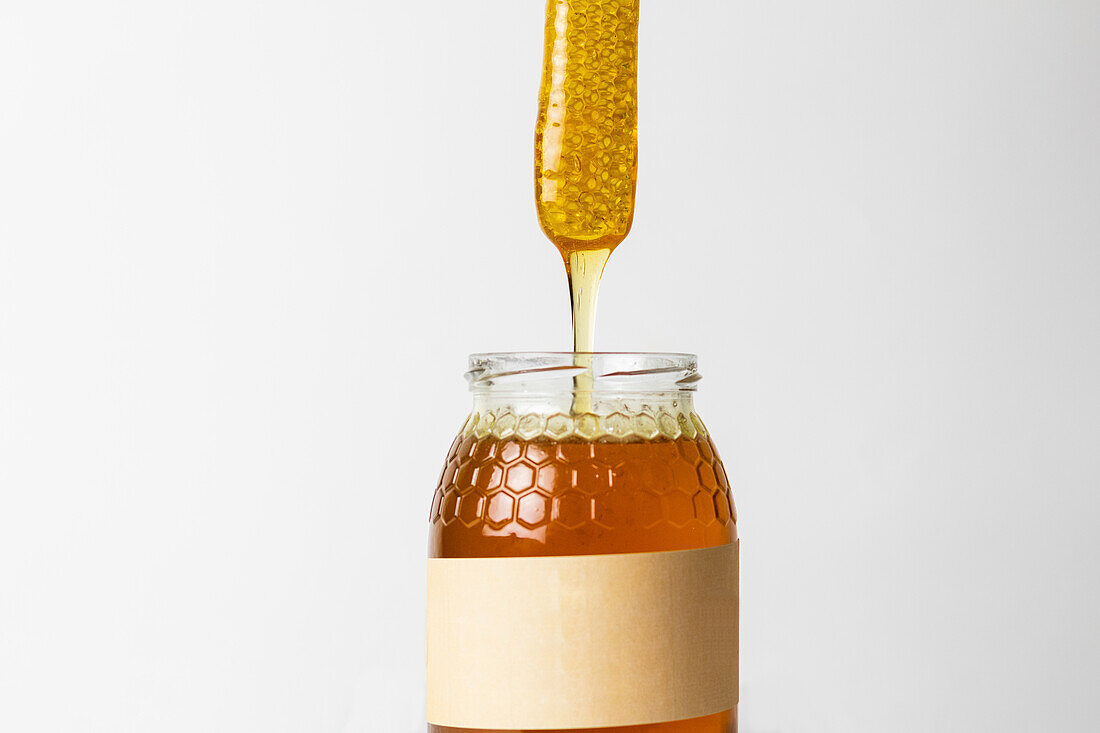 Piece of honeycomb on top of glass jar full of fresh natural golden honey with white background