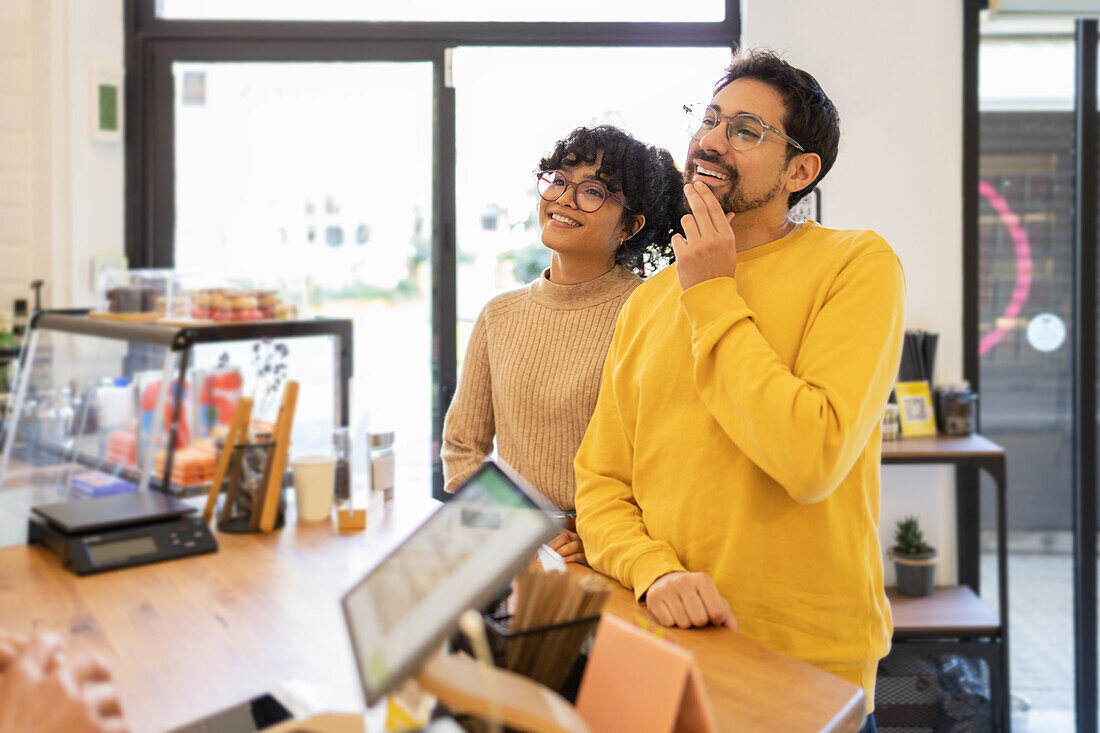 A happy and stylish young multiethnic couple is seen contemplating a purchase in a cozy and modern boutique.