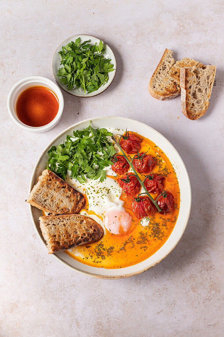 A plate of Turkish Eggs, featuring poached eggs atop Greek yogurt with garlic, seasoned with salt, pepper, and ginger powder, surrounded by cherry tomatoes and parsley