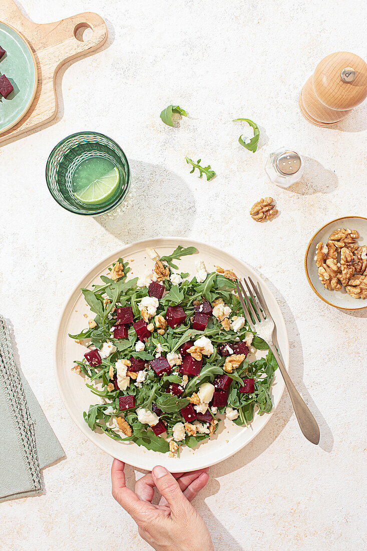 A beautifully arranged arugula salad with goat cheese, walnuts, and beetroot on a beige ceramic plate. Natural light enhances the vibrant colors and textures, creating a fresh and appealing scene