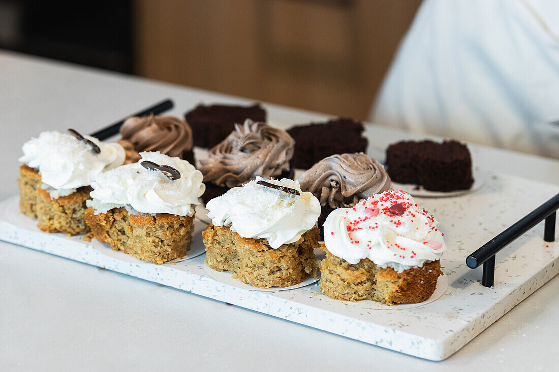 From above of carrot cakes with whipped cream placed with assorted vegan desserts on tray in bakery