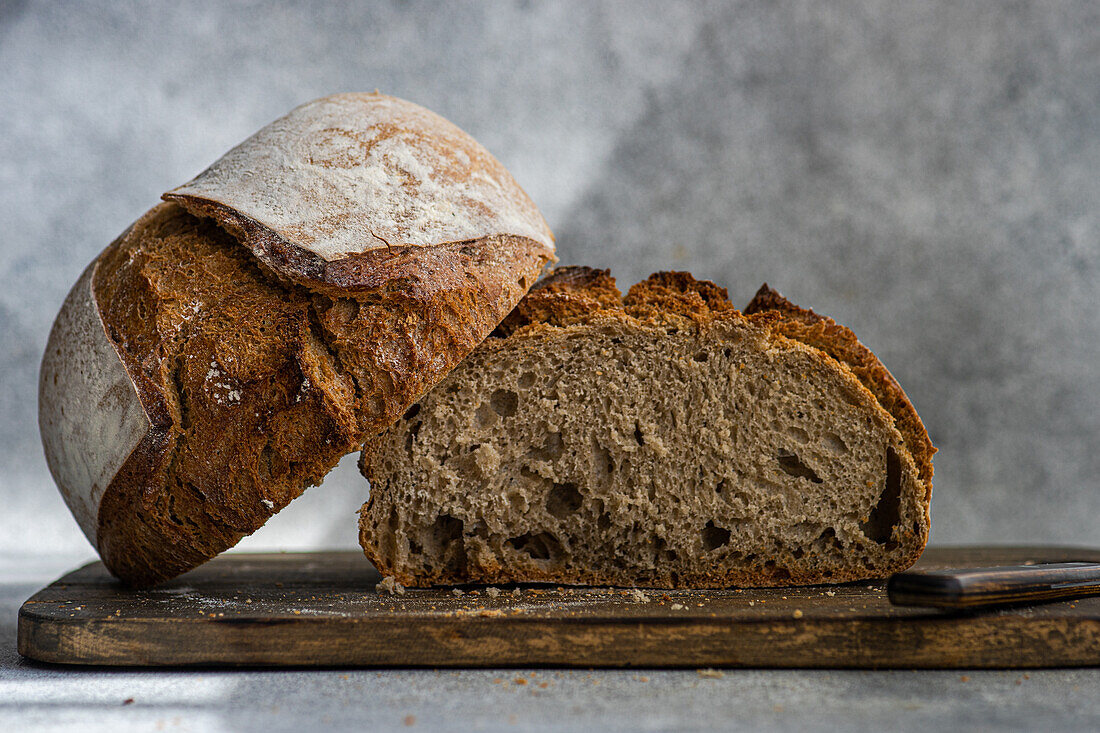 A loaf of homemade rye sourdough bread, sliced open to reveal its airy texture, sits on a rustic wooden cutting board with a knife beside it