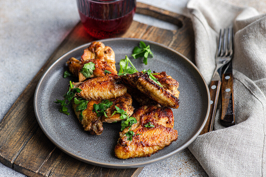 Succulent roasted chicken wings glazed in a spicy sauce, garnished with fresh coriander leaves, paired with a cherry cocktail, all served on a rustic plate.