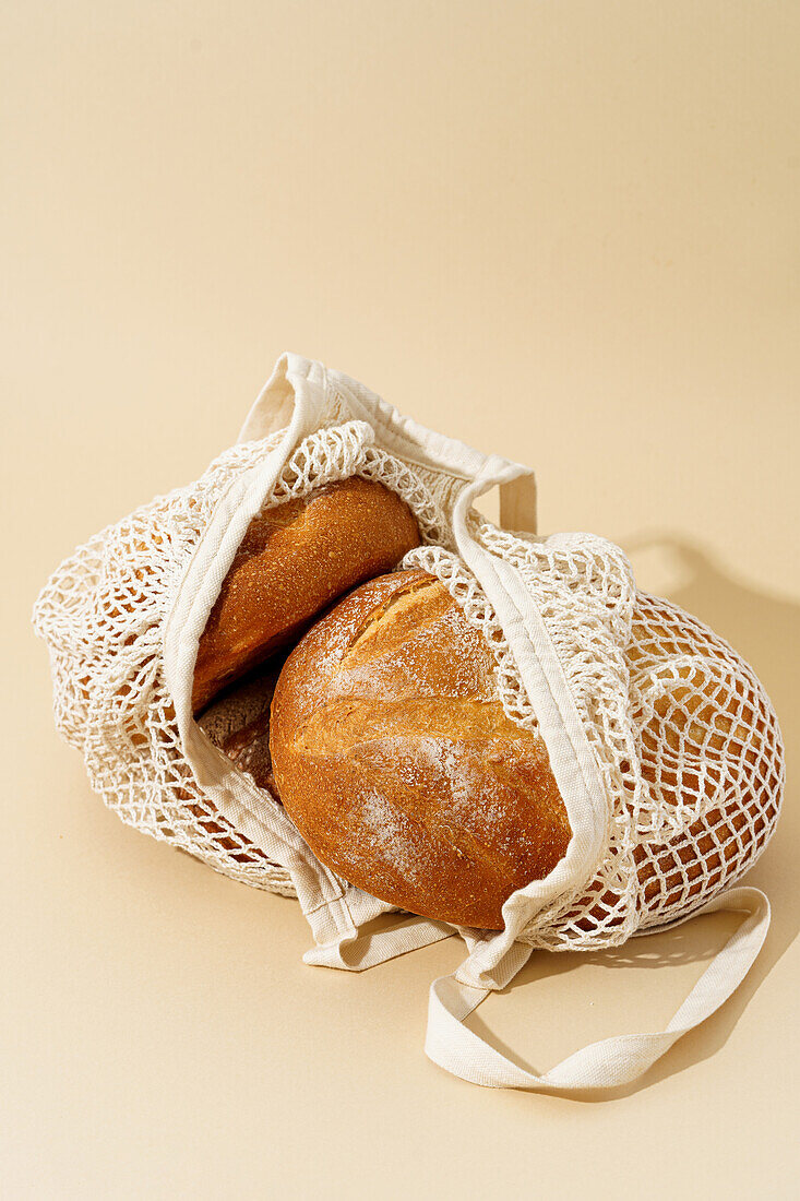 Various sourdough breads nestled in a woven reusable bag, promoting eco-friendly packaging against a soft beige background.