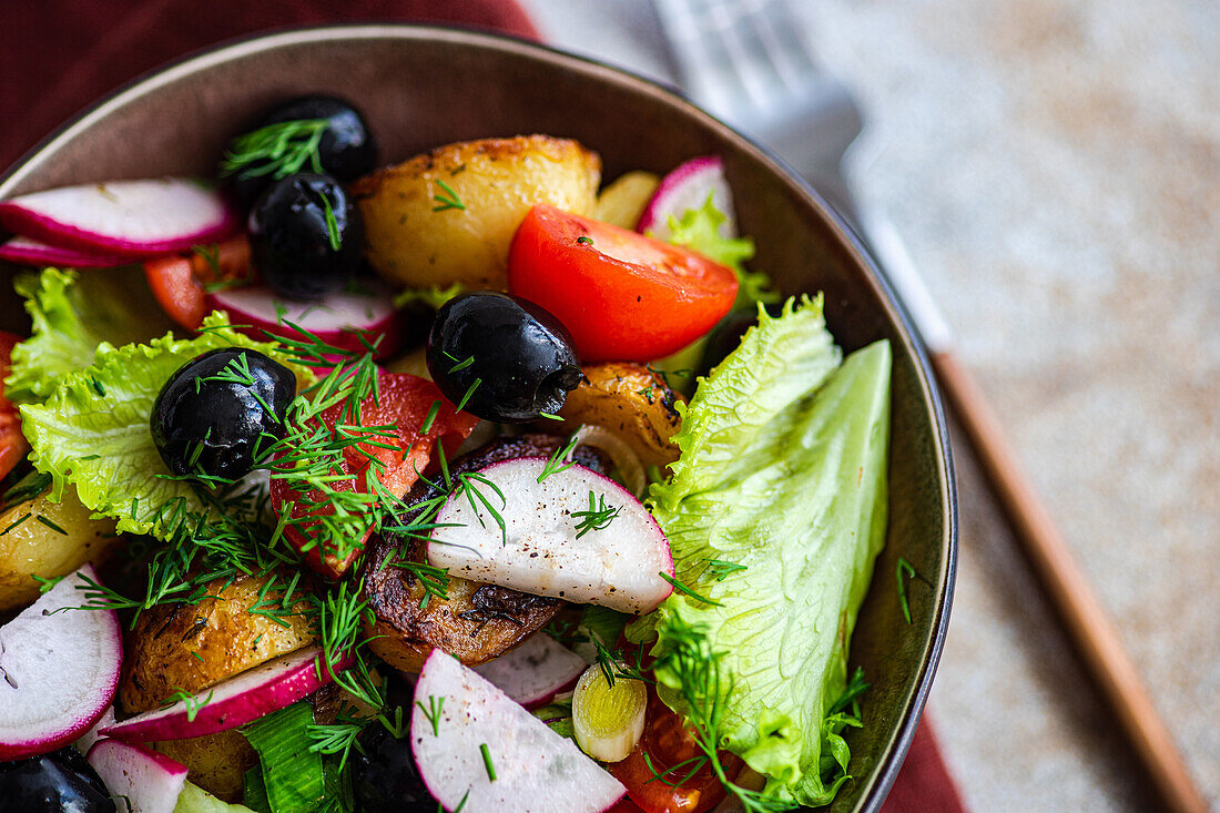 A close-up of a delicious Mediterranean salad bowl, with golden potatoes, ripe cherry tomatoes, black olives, spring onions, radishes, and lettuce, tastefully garnished with dill