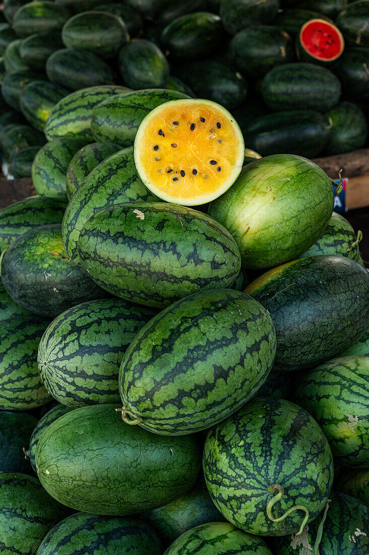 Auf einem traditionellen vietnamesischen Straßenmarkt werden gelbe Wassermelonen angeboten, von denen eine aufgeschnitten wird, um ihr saftiges, gelbes Fruchtfleisch zu zeigen.