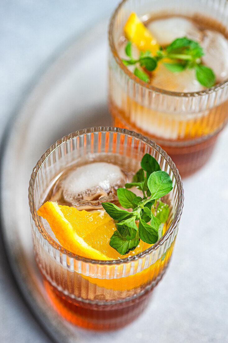 Ein belebender Sommercocktail mit Kirschlikör, gemischt mit Tonic, serviert in einem stilvollen Glas mit Eiswürfeln, verziert mit einer frischen Orangenscheibe und Minzblättern für einen lebendigen, erfrischenden Geschmack