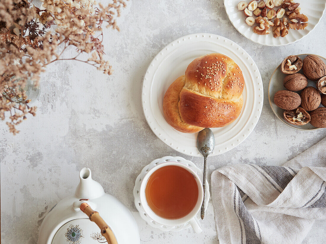 Heitere Herbstteeszene von oben mit frisch gebackenem Challah-Brot, einer dampfenden Tasse Tee und einer Auswahl an Walnüssen und Haselnüssen