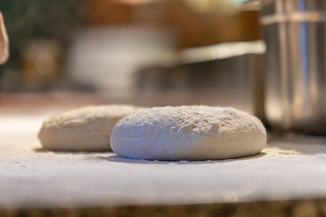 This image captures the early stage of pizza preparation, showing raw dough sprinkled with flour, ready for shaping and baking