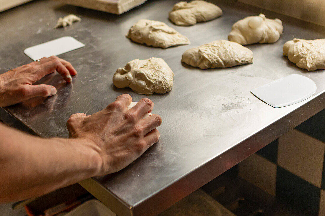 A person kneading fresh dough on a stainless steel table, preparing for pizza creation The image captures the hands in motion, emphasizing the art of handmade food