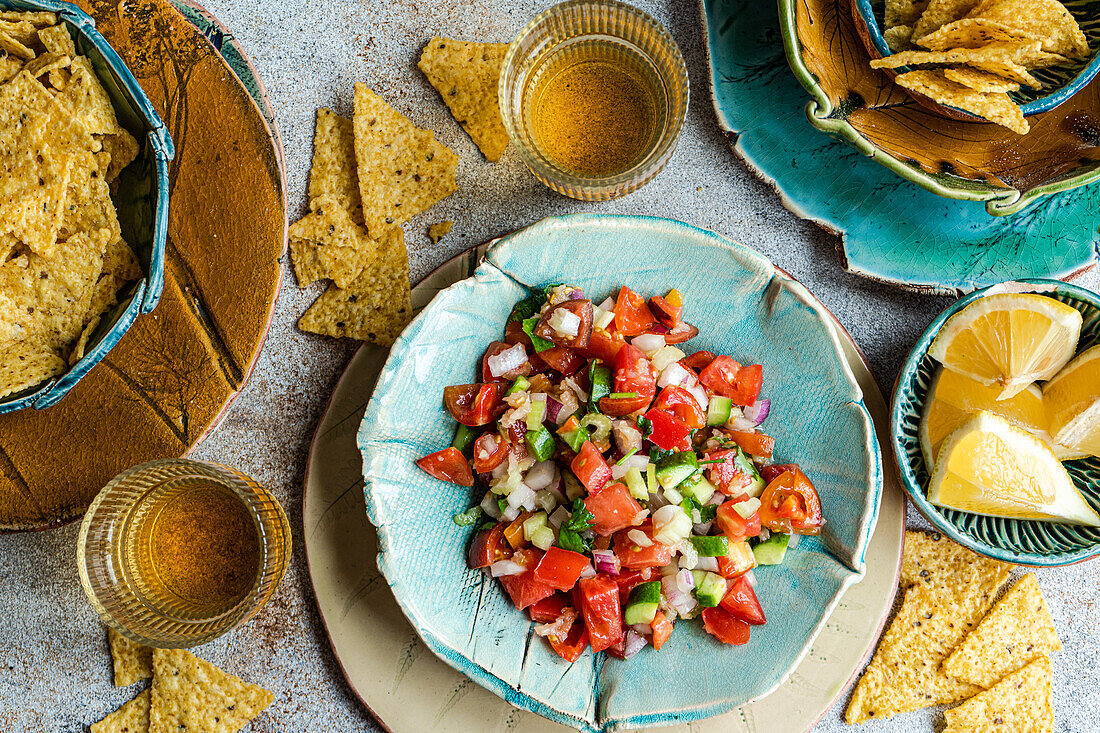 From above of traditional Mexican pico de gallo made with fresh tomatoes, onions, cilantro, jalapeños, and a dash of lemon juice, perfectly served alongside crispy corn tortilla chips on artisanal ceramic plates