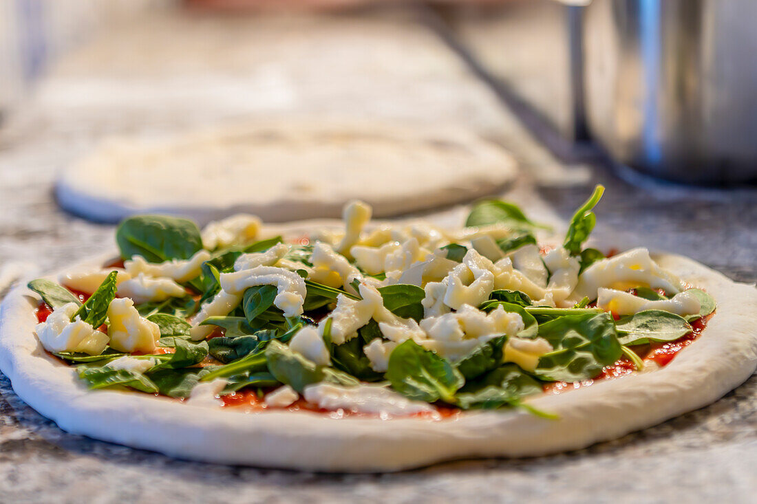 An uncooked pizza topped with fresh spinach leaves and chunks of mozzarella cheese, ready for baking The dough lies on a kitchen counter illuminated softly by ambient light