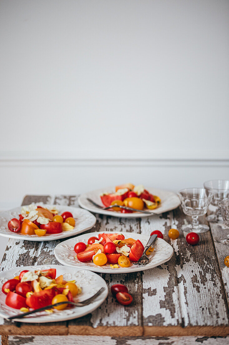 Three plates of vibrant tomato salad with cherry tomatoes on a weathered wooden table, portraying a refreshing summer meal