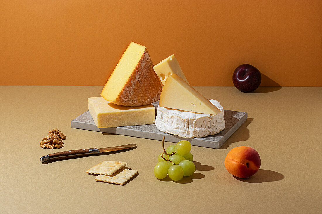 From above, variety of fine cheeses paired with fresh fruits, nuts, and crackers on a warm-hued backdrop