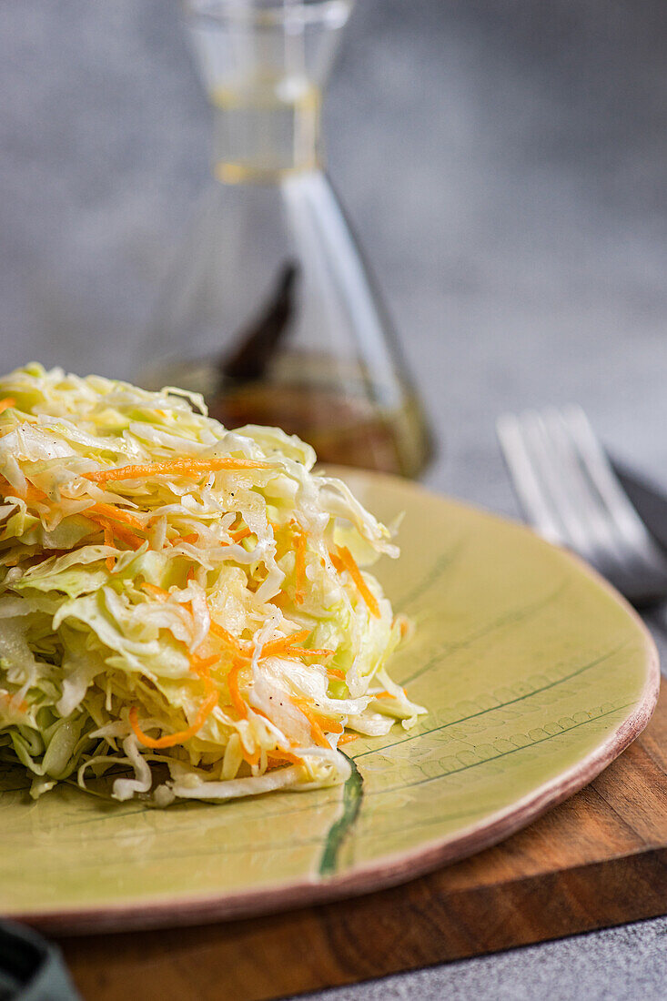 Healthy organic cabbage and carrot salad, drizzled with olive oil and served on a ceramic plate placed on a wooden board.