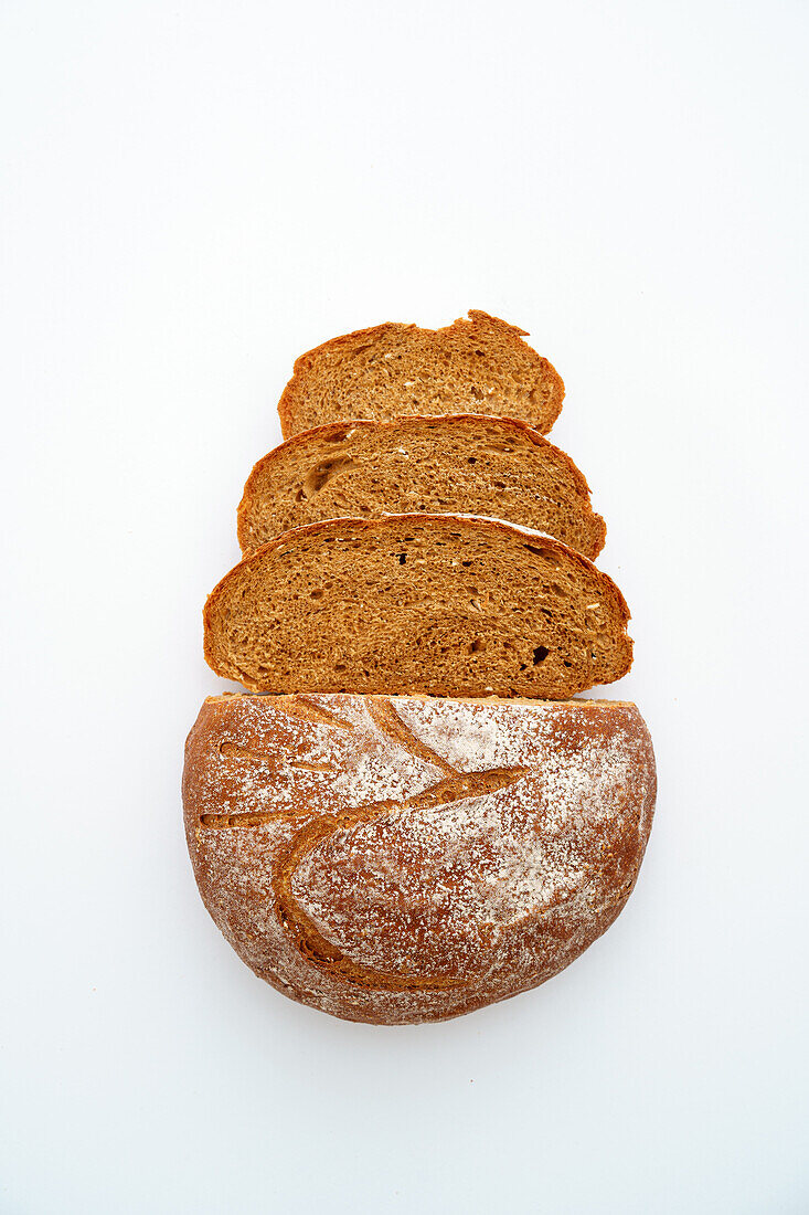 A whole loaf of sourdough rye bread and slices arranged in a row against a white background, showcasing the texture and crust.