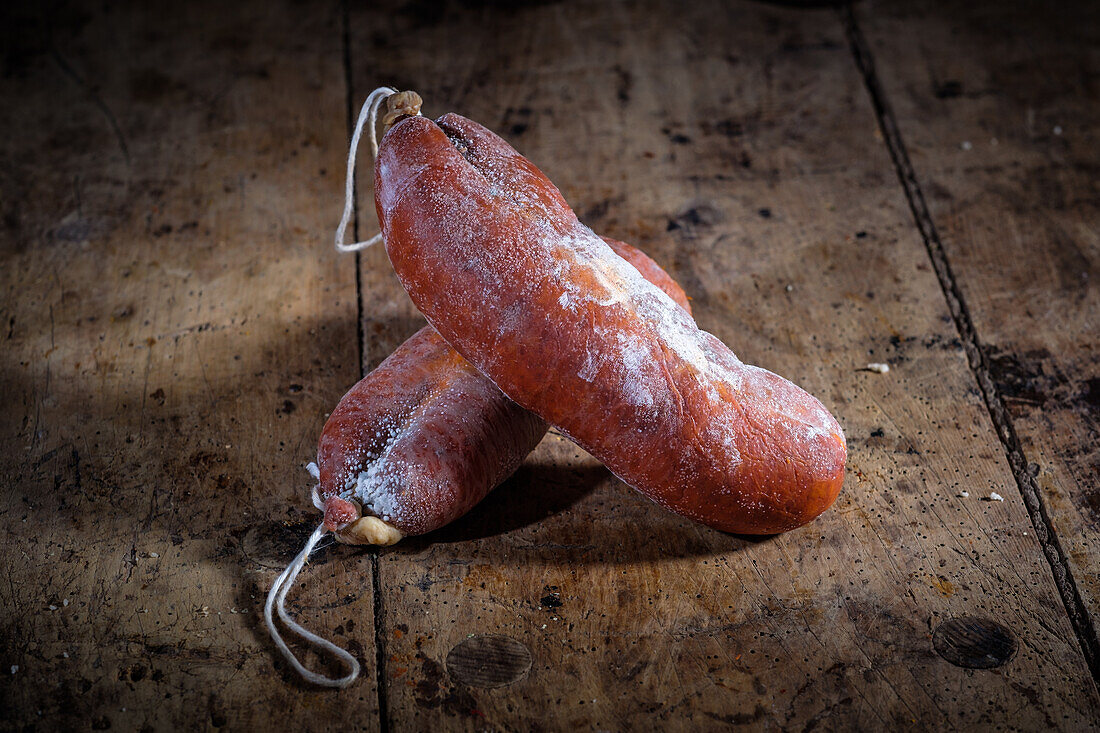 Zwei traditionelle Sobrasada-Würste, eine Spezialität der Balearen, liegen auf einem alten Holztisch. Die Würste haben eine kräftige Farbe, die auf ihren Paprikaanteil hinweist.