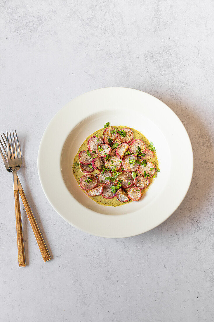 Overhead shot of a healthy dish with sliced roasted radishes drizzled with green tahini sauce on a white plate.