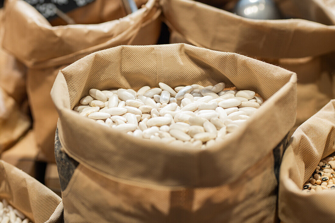 Close-up image of bulk white beans in a burlap sack with other grains in the background at an organic market