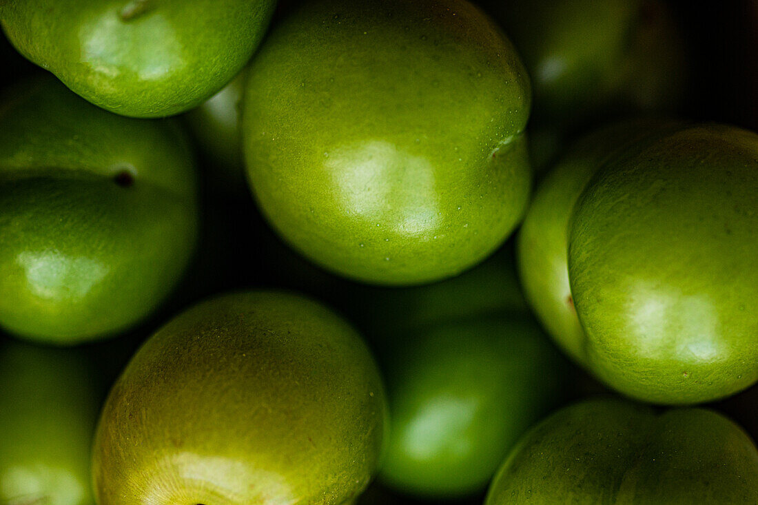 A close-up image of fresh, organic green plums piled in a bowl, commonly used in culinary traditions of regions like Georgia, Turkey, and Greece