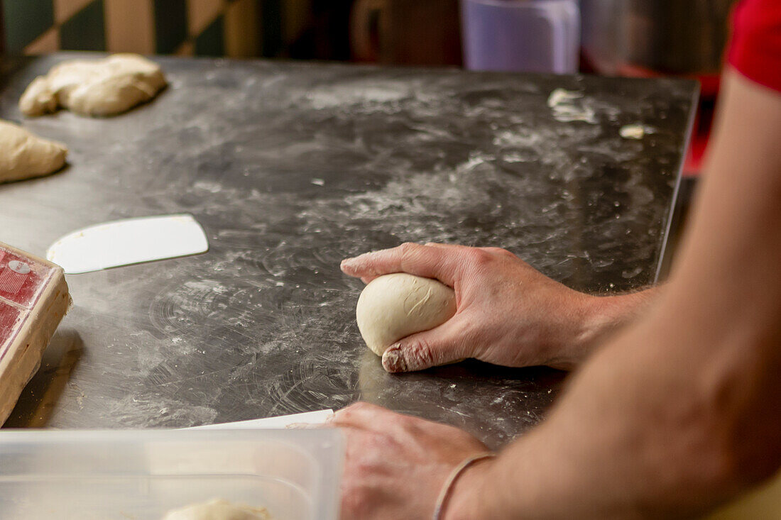 A professional cook shapes fresh pizza dough on a floured surface, focusing on creating a perfect base for pizza