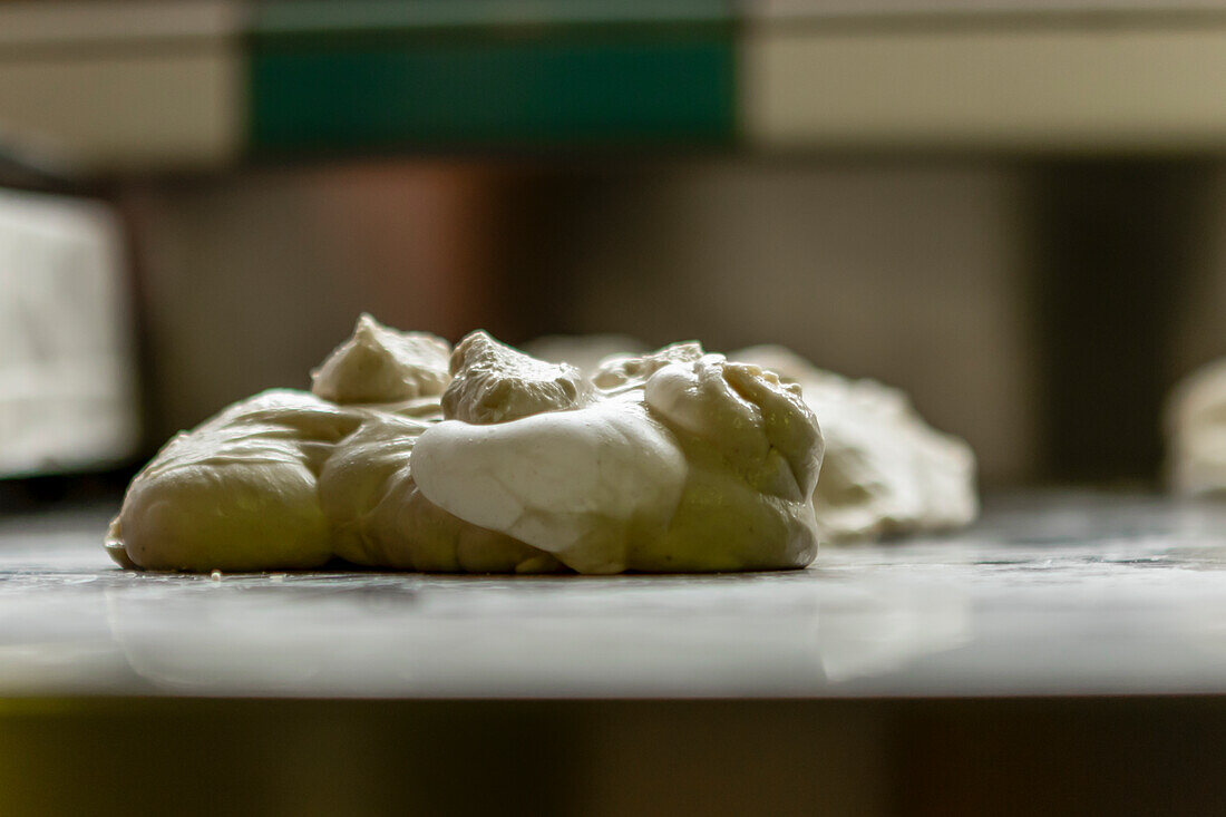 This image captures a close-up view of fresh, uncooked pizza dough on a metal kitchen counter, emphasizing the texture and details of the dough