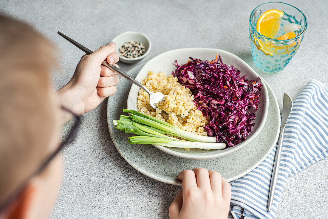 A bowl of wholesome food featuring a colorful raw red cabbage and carrot salad next to fluffy boiled bulgur, served with fresh green onions