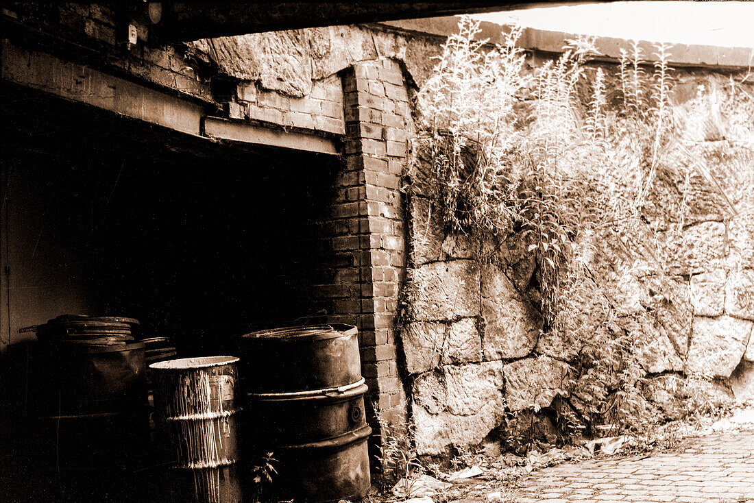 Old, Decomissioned & Obsolete Oil Drums, stacked away in a driveway for waste disposal inside the former DDR town of Chemnitz, just after Die Wende 1991. Shot on Analog Black & White Film. Former Karl Marx Stadt, Germany.