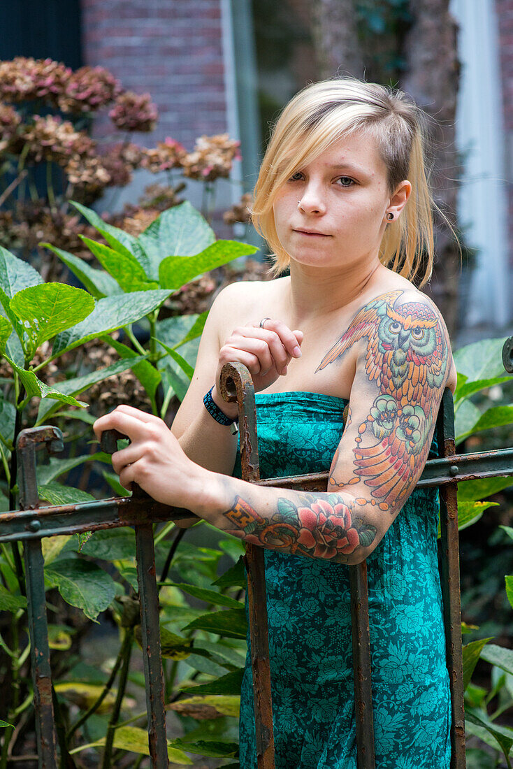 Porträt Junge Frau mit Tatoos im Wohngarten. Tilburg, Niederlande.