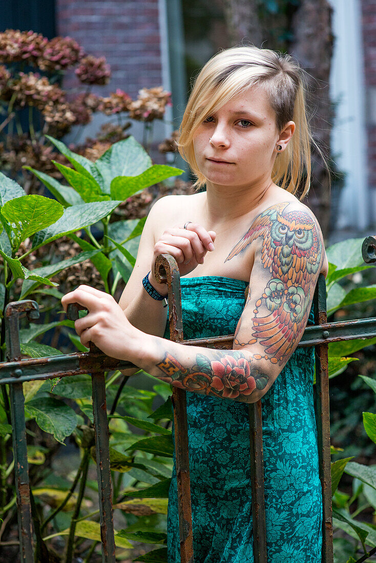 Portrait Junge Frau mit Tatoos im Wohngarten. Tilburg, Niederlande.