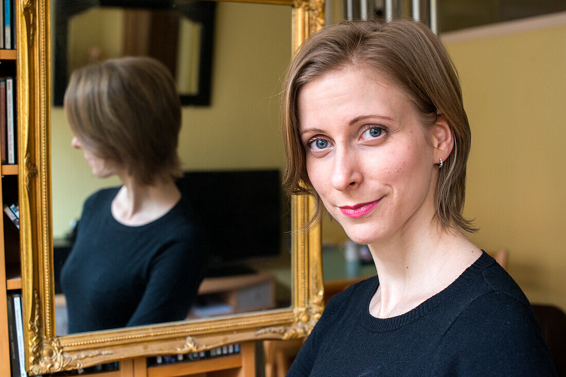 Tilburg, Netherlands. Young adult caucasian woman showing the results of a make up session, using a living room mirror.