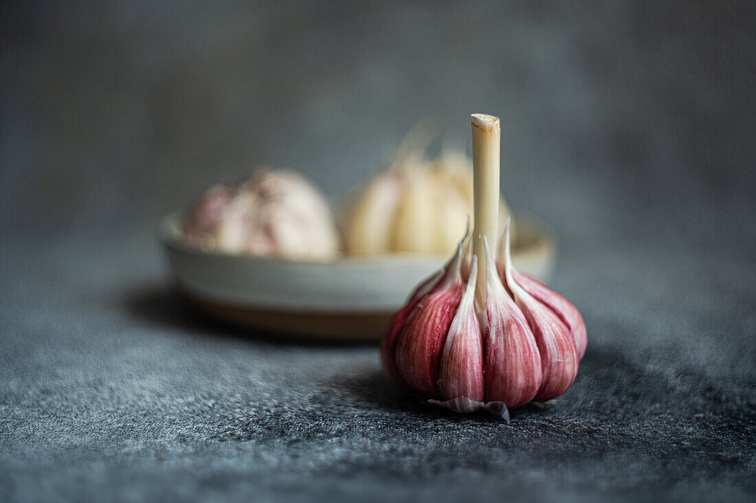 A close-up view of fresh garlic bulbs arranged thoughtfully on a textured, dark surface, highlighting each bulb’s unique texture and natural pink hue