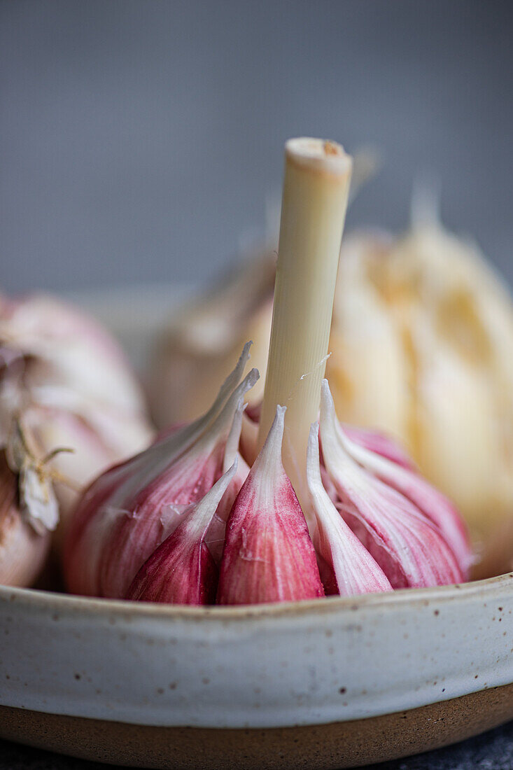 A detailed image showing several garlic cloves presented in a rustic ceramic bowl on a neutral background The shot emphasizes the natural textures and colors of garlic, ideal for cooking and culinary themes