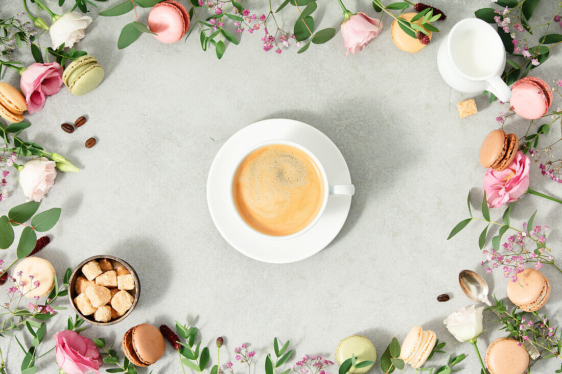 Weiße Kaffeetasse und Rahmen aus Frühlingsblumen und verschiedenen Makronensorten flach gelegt