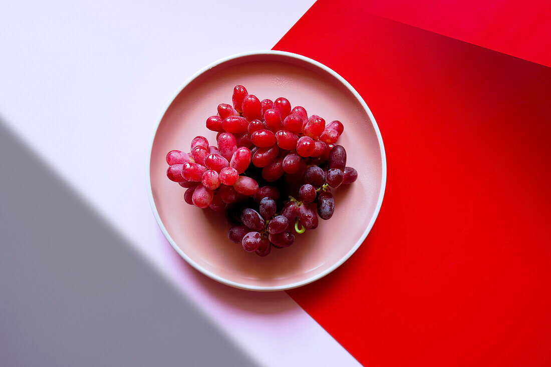 Rote Weintrauben mit Color Blocking und geometrischer Schattenästhetik.