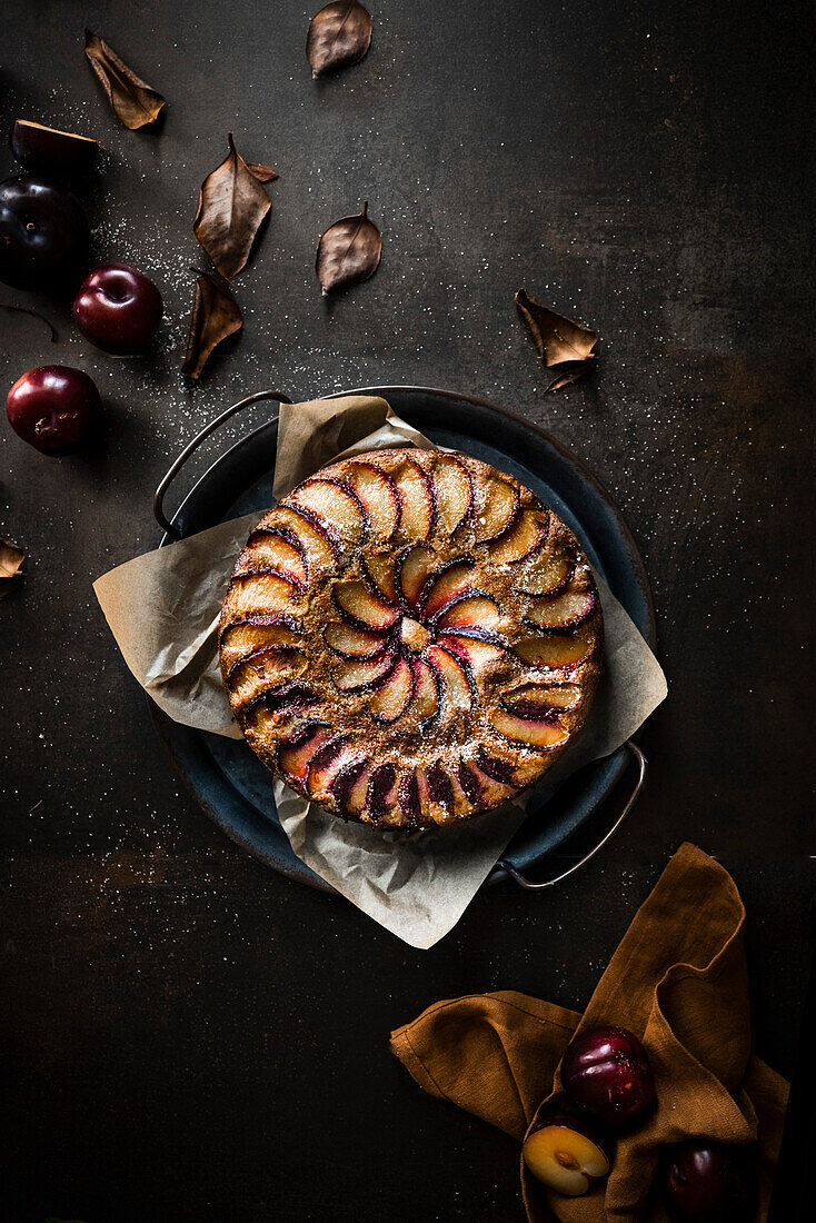 A rustic plum cake surrounded with autumn leaves and fresh fruit