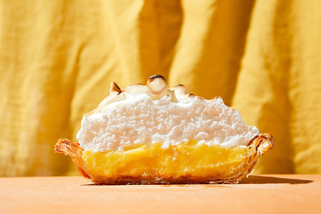 Lemon meringue pie with bright hard light on an orange foreground and yellow backdrop