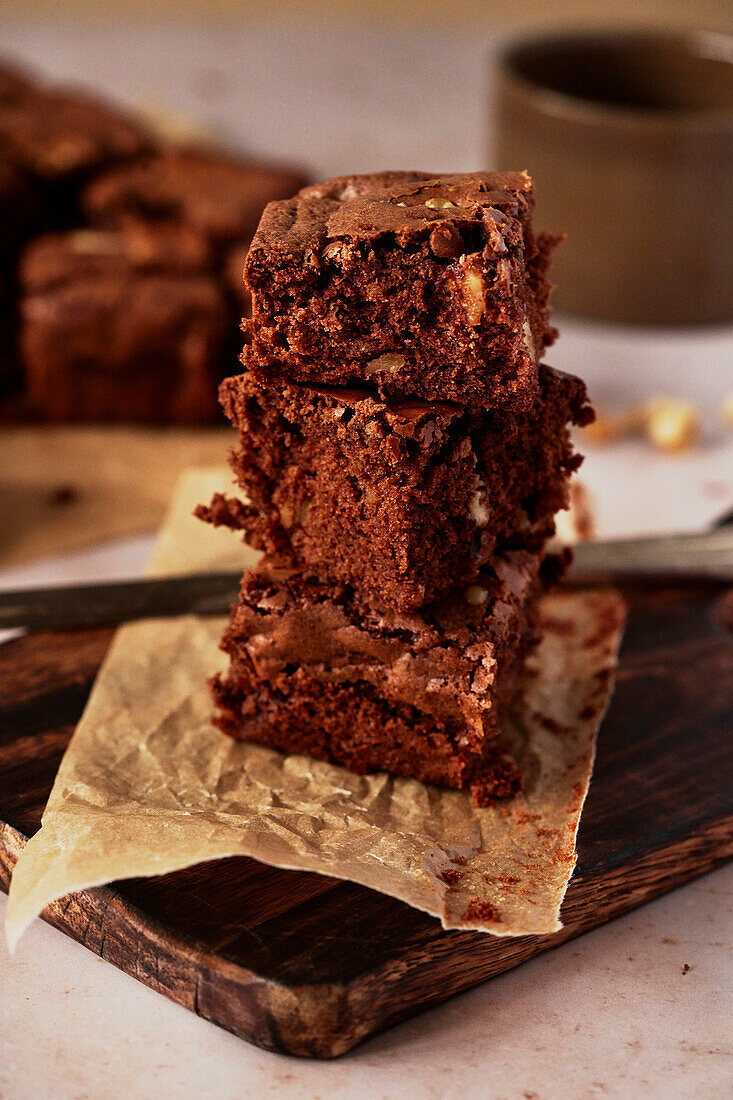 Slices of brownie on a wooden board, stacked with a knife and a teacup