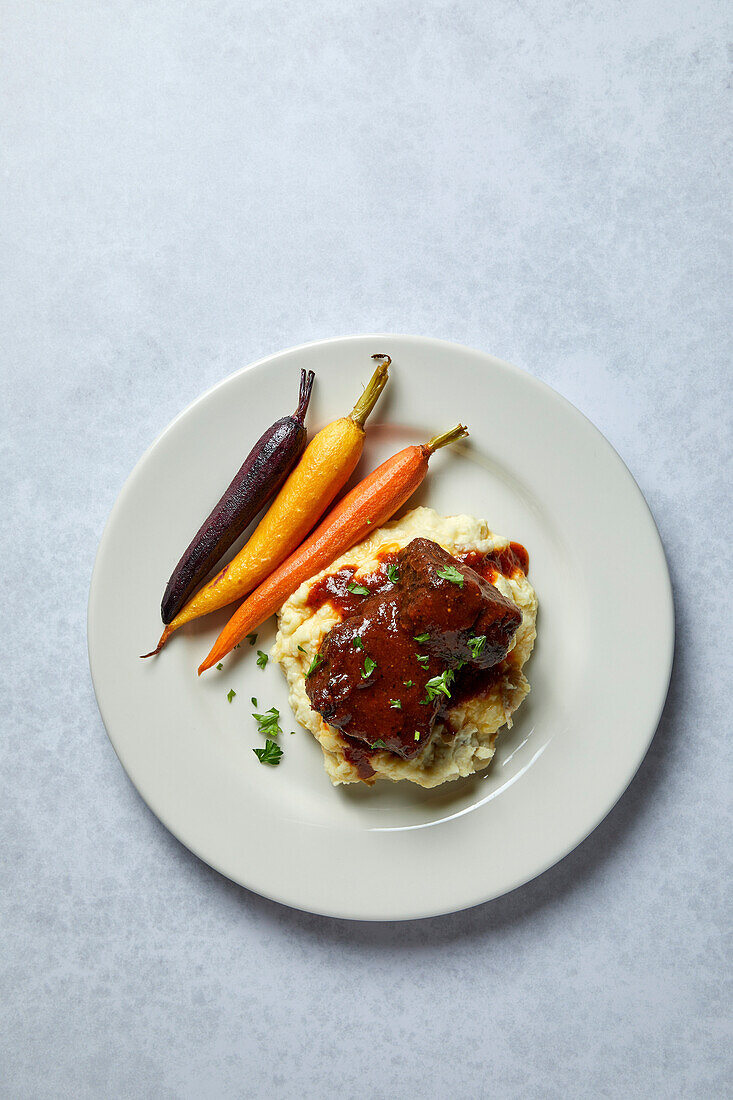 Beef Short Ribs with Mashed Potatoes and Rainbow Carrots on a Neutral Background with Soft Shadows