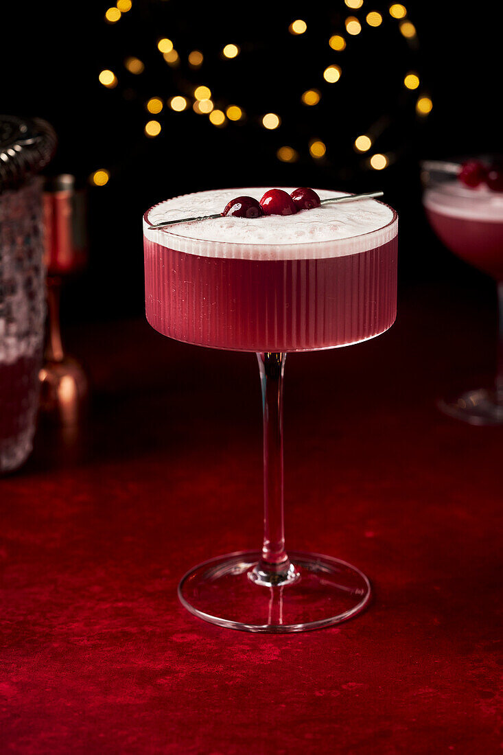 Mulled Wine Sour with Cranberries on Red Surface with fairy lights and glasses