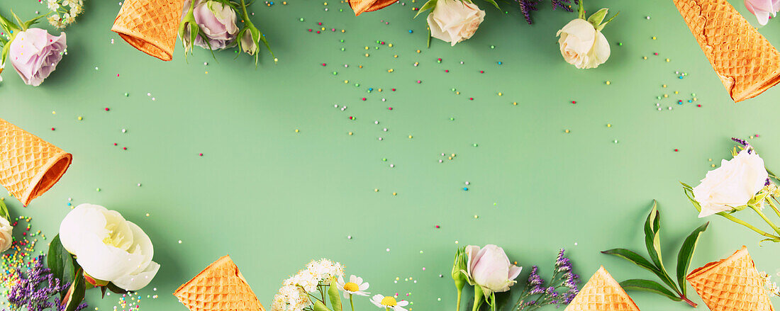 Flat lay of waffle cones and flowers on a pastel green background, top view, flat lay. Spring or summer mood concept, banner, copy space