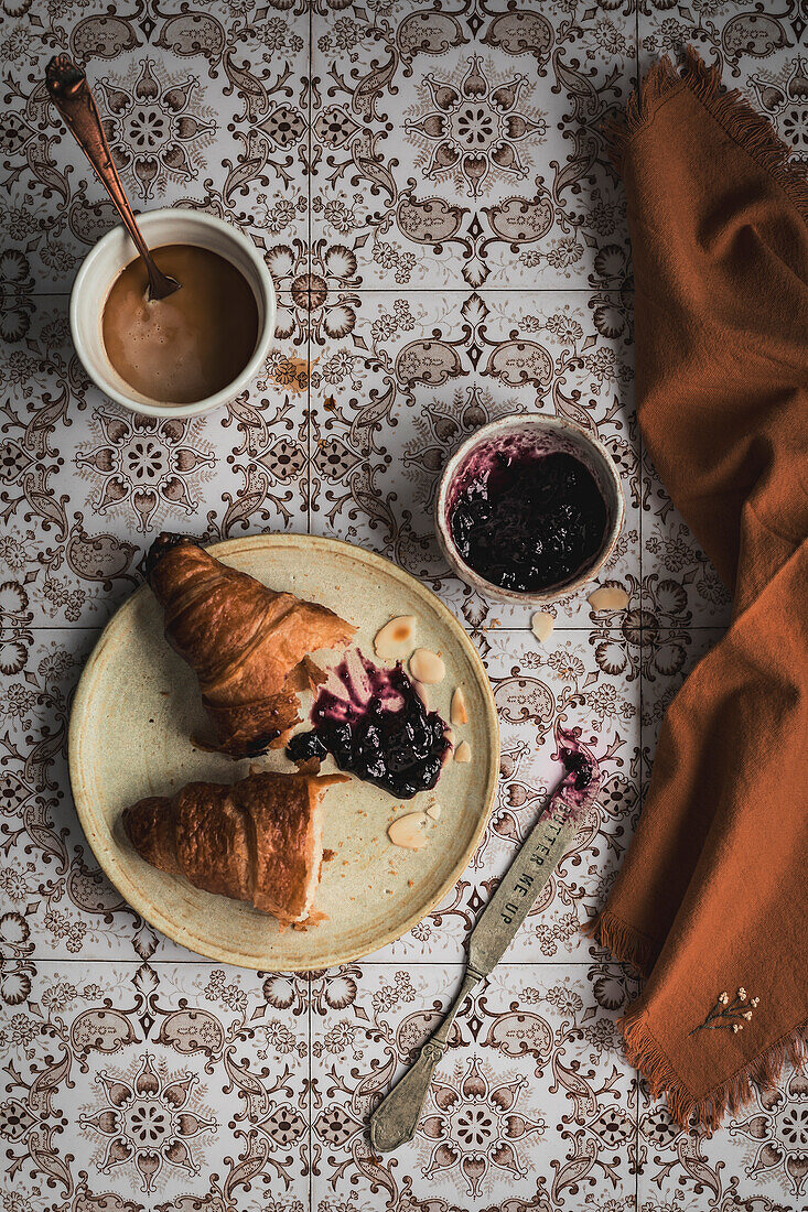 A breakfast scene, an espresso, a croissant and blueberry jam and granola.