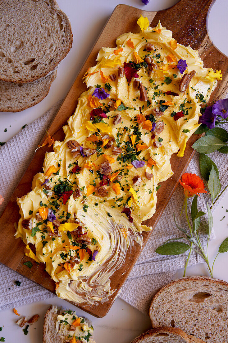 Butterbrett mit Kräutern, Pekannüssen und essbaren Blumen in Großaufnahme.