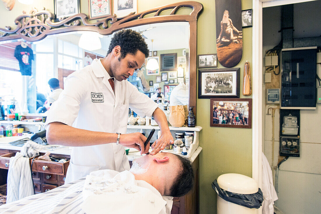 Professioneller Barbier und Haarschneider rasiert seinen Kunden im Schorem Barber Shop am Nieuwe Binnenweg, Rotterdam, Niederlande.