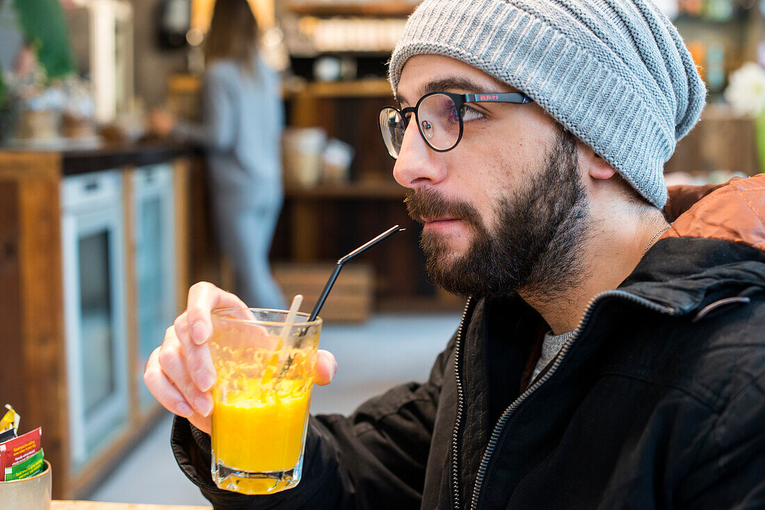 Tilburg, Niederlande. Porträt eines Brillenträgers in einer Kantine und einem Restaurant, der Orangensaft trinkt.